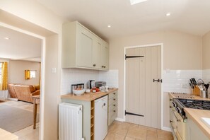 A modern kitchen with a gas stove, white cabinets, and a dining area with a sofa and table. - 2 Bed in Bridport (oc-dc110) (Chideock)