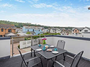 Eine Dachterrasse mit Tisch für zwei Personen, mit Blick auf ein Wohngebiet mit Häusern und Grünflächen.