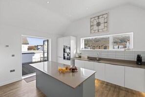 Cocina moderna con isla, horno integrado y grandes ventanales con vistas al exterior.
