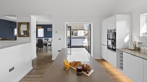 Moderni keittiö, jossa on keskeinen saareke, ruokailutila pöytineen ja tuoleineen sekä näkymä ulos.