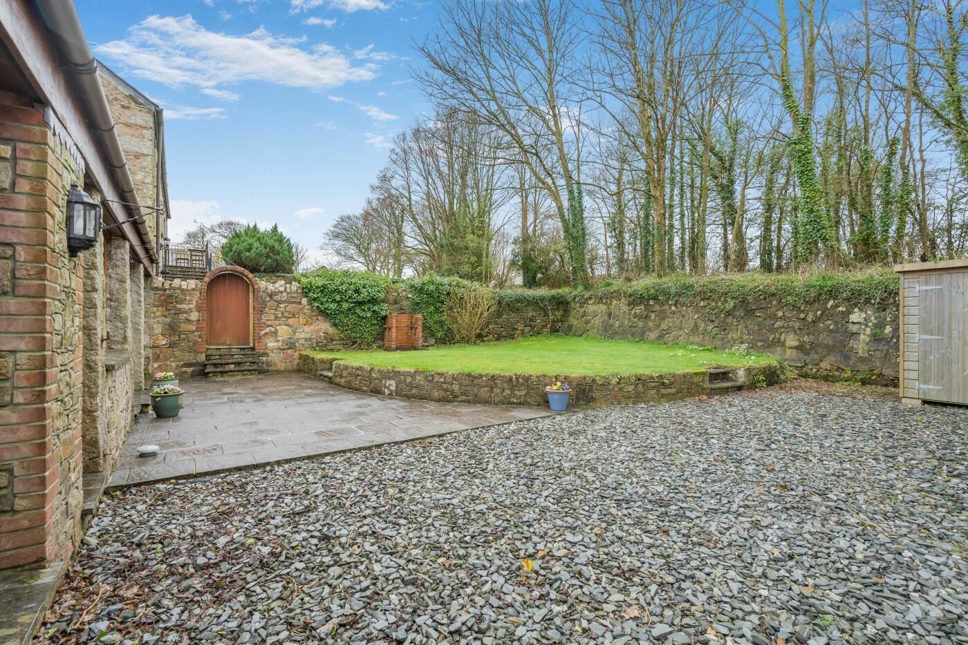 A courtyard with a stone wall, a grassy area, and a gravel path.