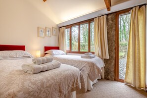 Camera d'albergo con due letti, una testiera rossa, un'ampia finestra con tende e vista sul verde.