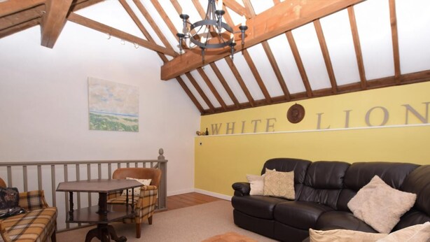 A room with a wooden ceiling, a black leather sofa, a plaid sofa, a small table, and a yellow wall with 'WHITE LION' text. - 2 Bed in Holt (oc-73335) (Holt)