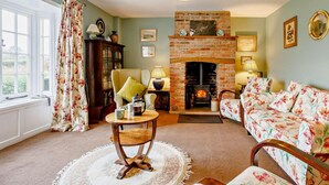A cozy living room with a fireplace, a sofa, a table, and a bookshelf. - 4 Bed in Dorchester (oc-dc190) (Winfrith Newburgh)