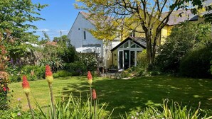 A well-maintained garden with a lawn, flowering plants, and a small building with a glass door. - 4 Bed in Dorchester (oc-dc190) (Winfrith Newburgh)
