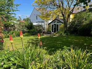 Ein gepflegter Garten mit Rasenfläche, blühenden Pflanzen und einem kleinen Gebäude mit Glasdoor.