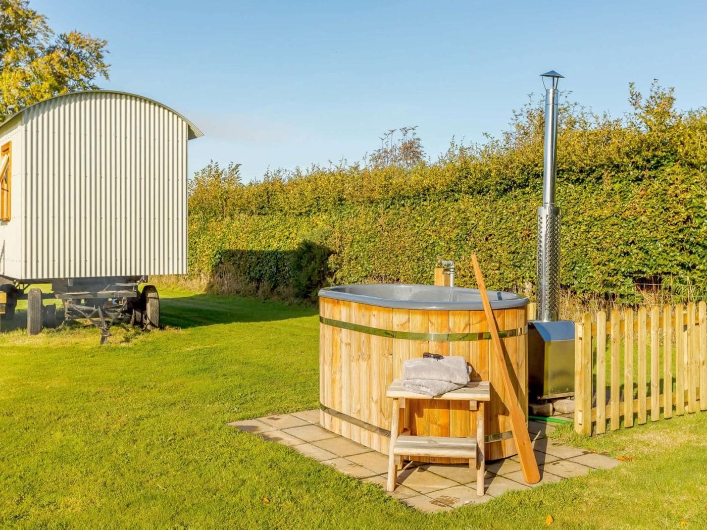 A hot tub with a wooden bench and a portable sauna unit in a grassy area with a wooden fence and a shed in the background.