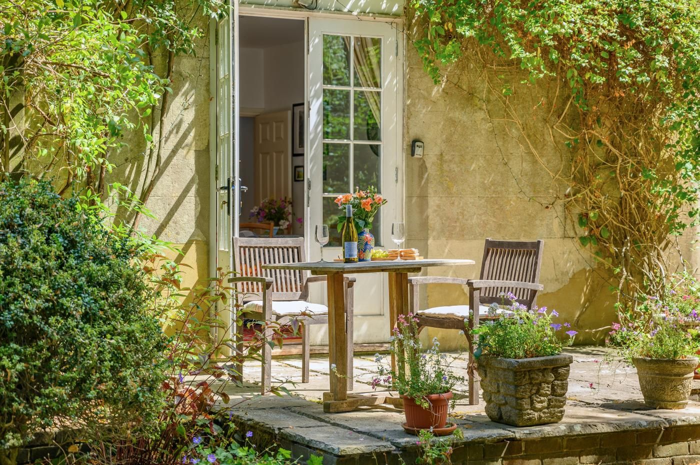 Eine Terrassensitzgruppe mit Tisch und Stühlen, umgeben von Grünpflanzen und Kübelpflanzen.