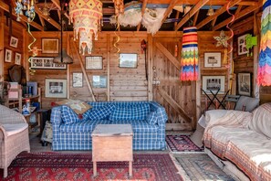 A cozy cabin interior with a checkered sofa, a small wooden table, and a variety of hanging decorations. - 1 Bed in Dorchester (oc-dc092) (Winfrith Newburgh)