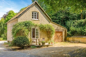 Ein Steinhaus mit Satteldach, einer Holztür und einer kleinen Veranda mit Tisch und Stühlen.