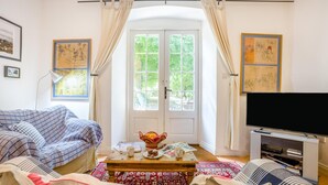 En stue med en sofa, et sofabord med en skål og en tallerken, et fjernsyn og en dør med gardiner.