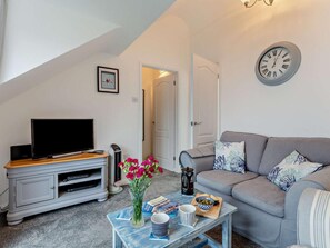 Ein Wohnzimmer mit Fernseher, Sofa, Couchtisch und einer Wanduhr.