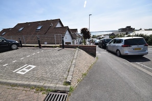 Ein Parkplatz mit asphaltiertem Belag, einem Abflussgitter und einem weißen Gebäude mit geneigtem Dach.