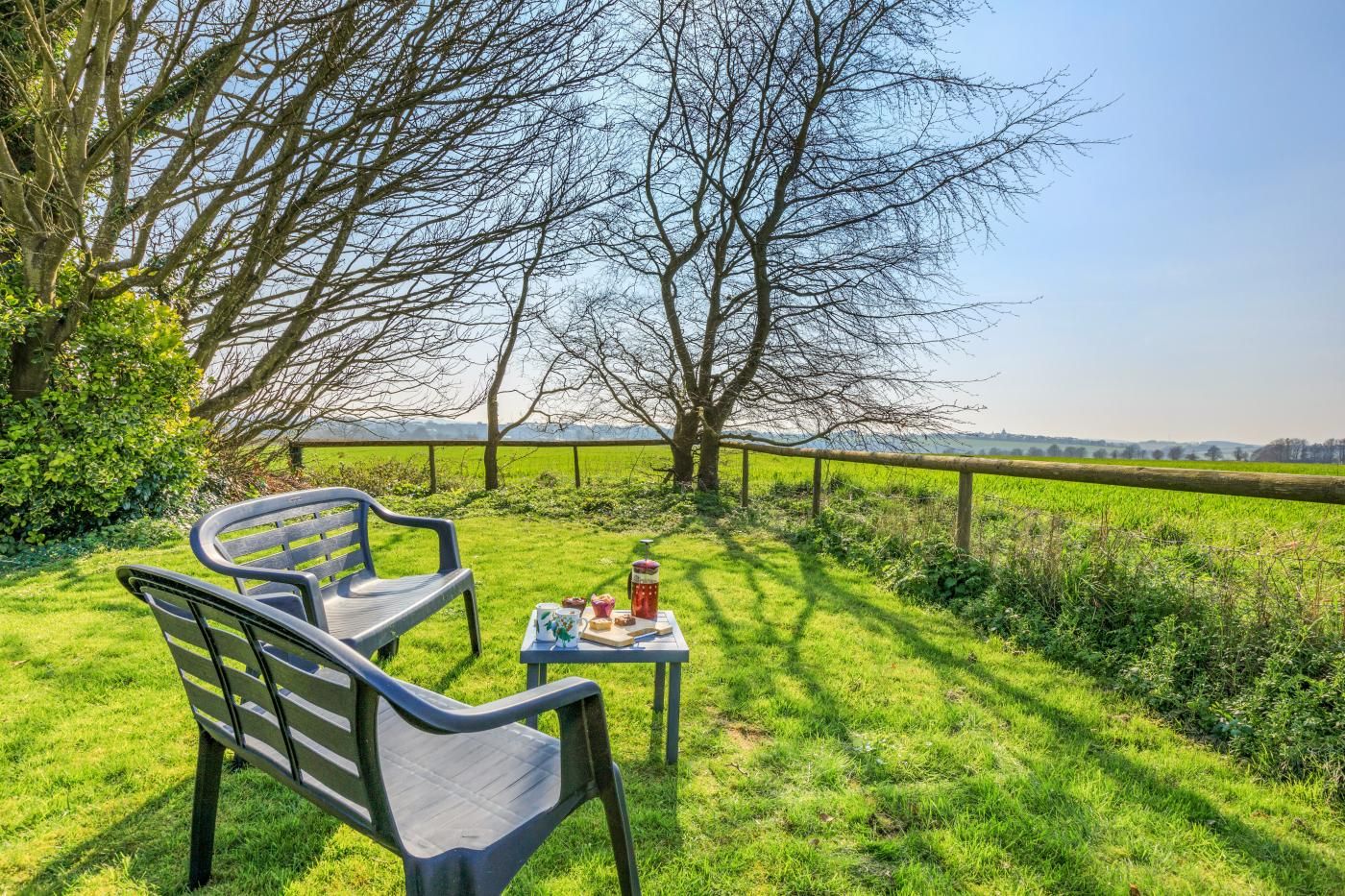 An outdoor seating area with a table and chairs, a grassy field, and a tree in the background.
