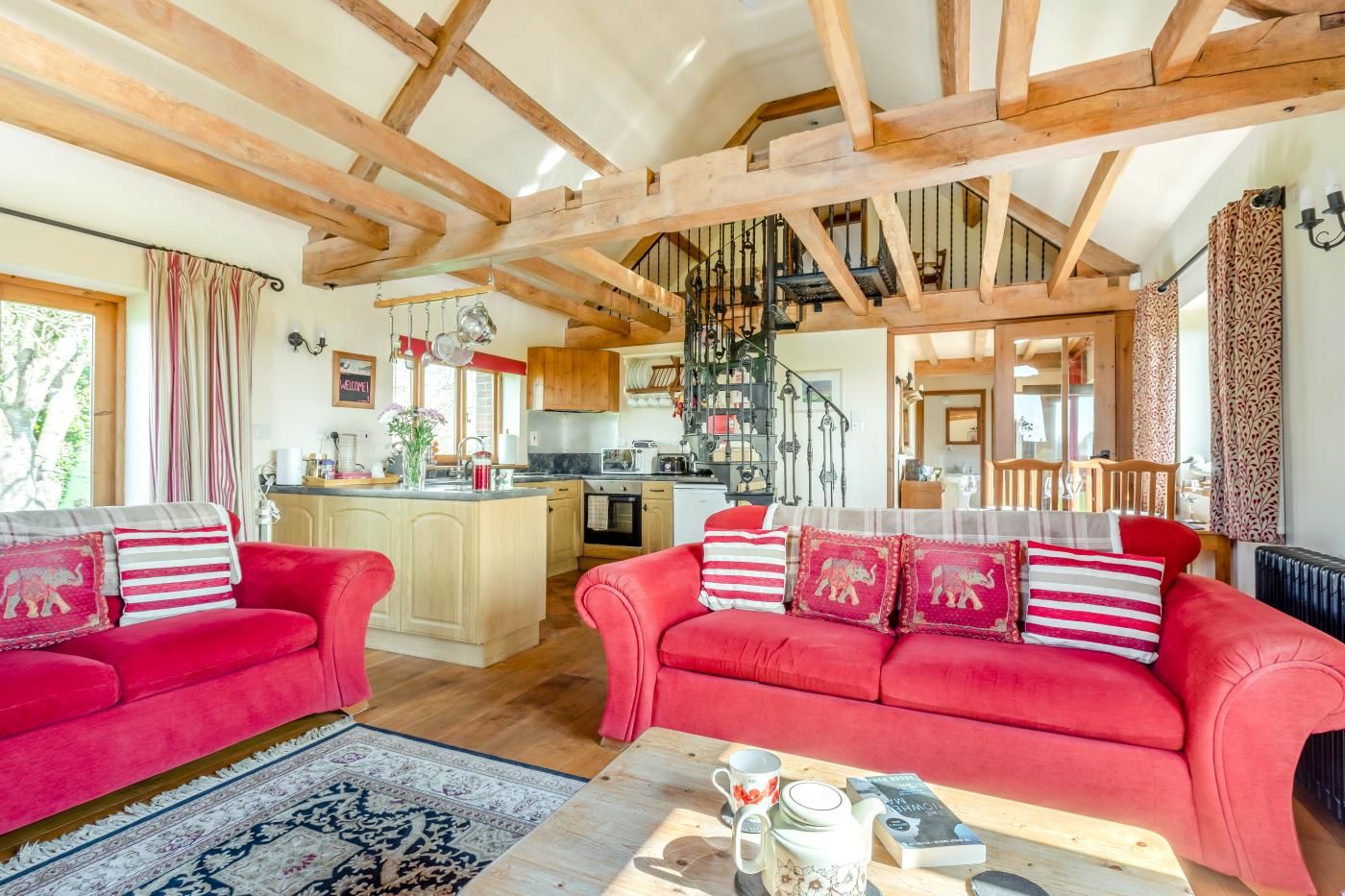 A spacious living area with a red sofa set, a coffee table, and a kitchen in the background.