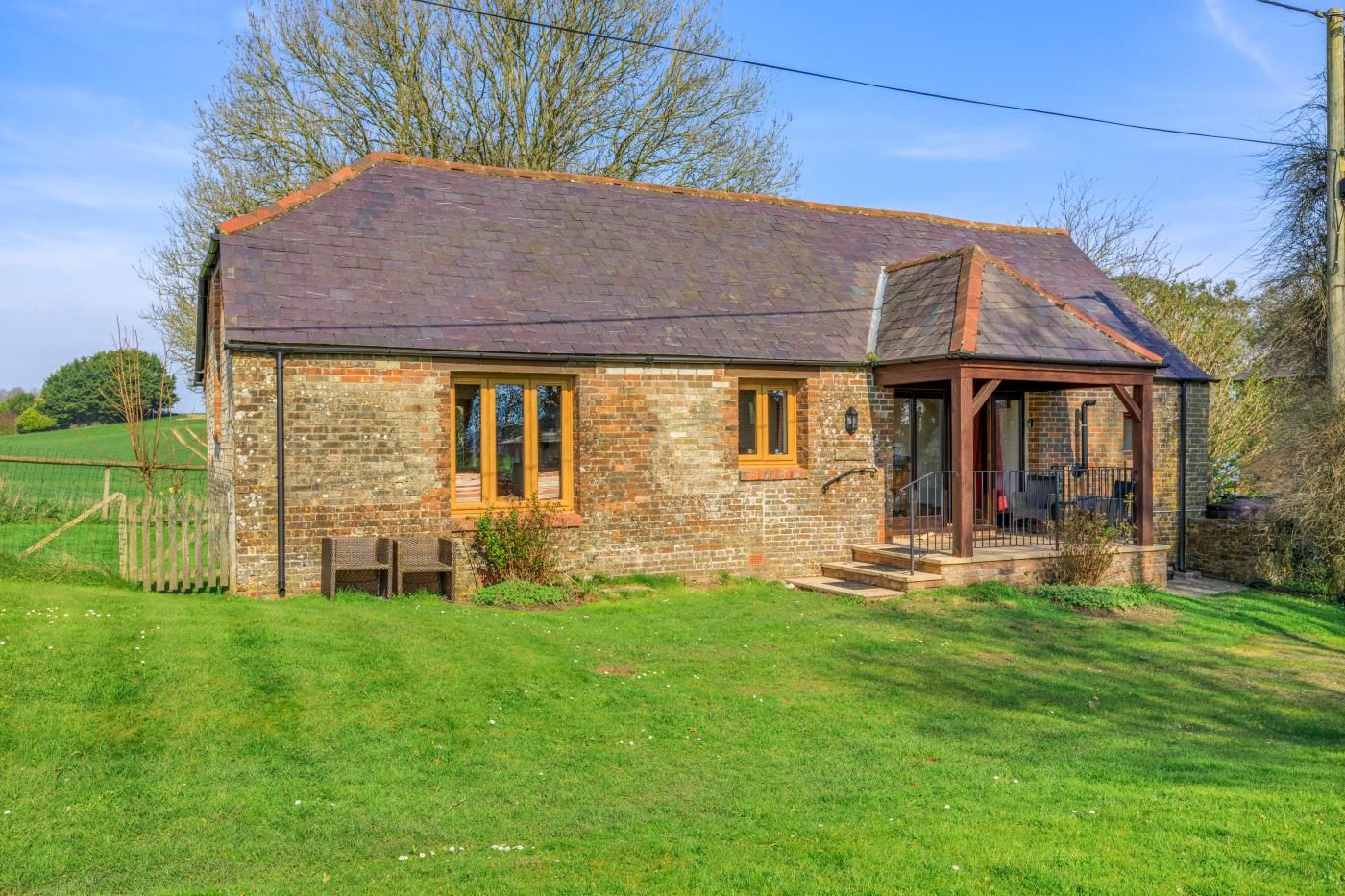 A stone building with a sloped roof, a porch with outdoor seating, and a fenced yard.