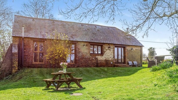 A brick building with a sloped roof, a picnic table, and a small garden area. - 2 Bed in Dorchester (oc-dc075) (Frome Whitfield)