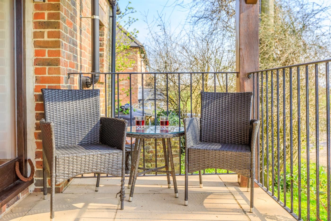 A patio with wicker furniture and a table, a brick wall, and a metal railing.
