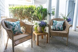 Two wicker chairs with patterned cushions, a small wooden table with a potted plant, and a gravel floor. - Ocean Lookout - Resort Stay with Pool & Hot Tub (Nanoose Bay)