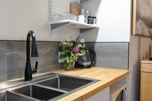 Ett kök med en modern blandare, en kaffebryggare och en hylla med glas och flaskor.