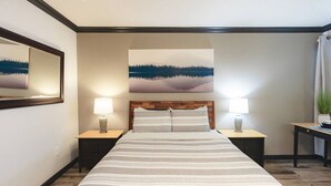 Quarto de hotel com uma cama, duas mesas de cabeceira, um abajur, um quadro e um vaso de planta.