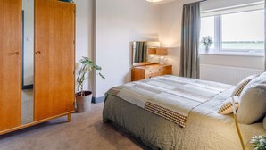 Et soveværelse med en seng, et skab, et natbord med lampe, en potteplante og et vindue med udsigt.