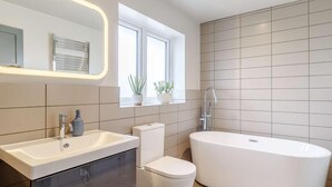 Et moderne badeværelse med et fristående badekar, et vaskeskrin med spejl og et toilet.