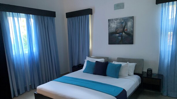A modern hotel room with a large bed, a nightstand, a painting on the wall, and blue curtains. - Royal Villa 4-bedroom Villa-January 15, 2027-January 22, 2027 (Cofresi)