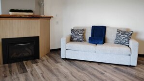 Ein Wohnzimmer mit einer Couch, gemusterten Kissen, einem Kamin und Holzboden.