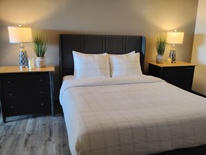 Ein Hotelzimmer mit einem großen Bett, zwei Nachttischen mit Lampen, einem dunklen Kopfteil und je einem kleinen Blumentopf auf jedem Tisch.