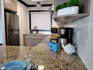 Eine Küche mit einer Granitabdeckung, Edelstahlgeräten, einer Kaffeemaschine und einem Blumentopf an der Wand.
