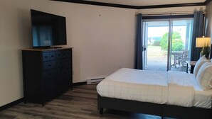 Ein Schlafzimmer mit Bett, Schminktisch, Fernseher und einer Glastür zu einem Außenbereich.