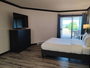 Ein Schlafzimmer mit Bett, Schminktisch, Fernseher und einer Glastür zu einem Außenbereich.