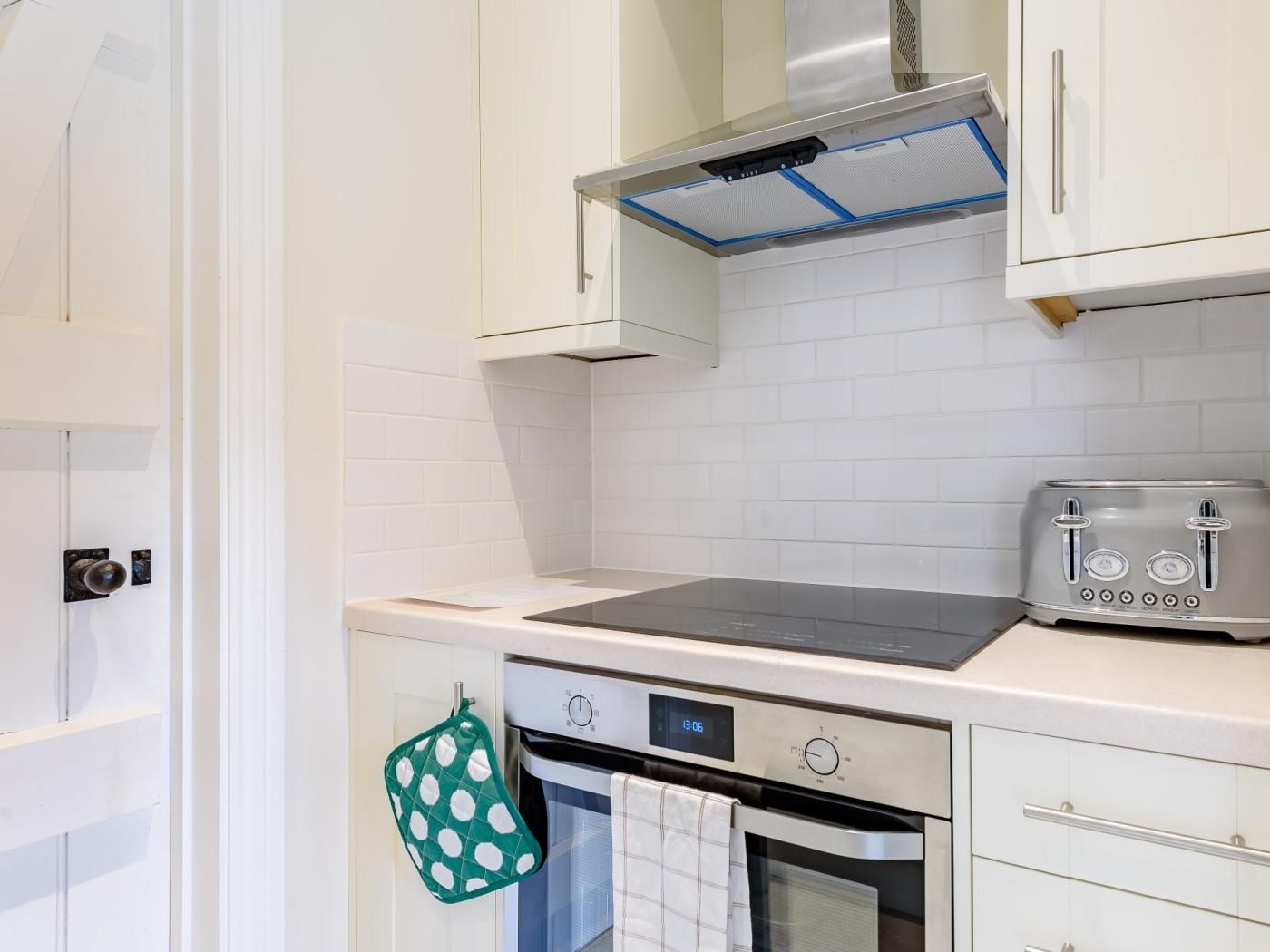 A kitchen with white cabinets, a stove, a toaster, and a digital clock displaying 13:06.
