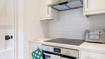 A kitchen with white cabinets, a stove, a toaster, and a digital clock displaying 13:06.