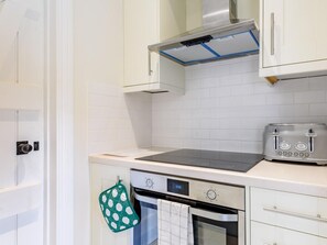A kitchen with white cabinets, a stove, a toaster, and a digital clock displaying 13:06. - 1 Bed in Manningtree (oc-78388) (Lawford)