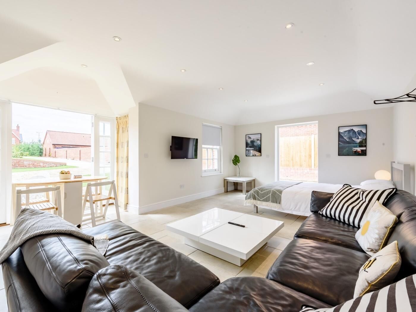 A spacious living room with a leather sofa, a coffee table, and a TV mounted on the wall.