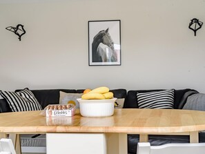 A dining area with a round table, a plate of bananas, a box of Crumble's big choc macarons, and a framed horse picture on the wall. - 1 Bed in Manningtree (oc-78388) (Lawford)