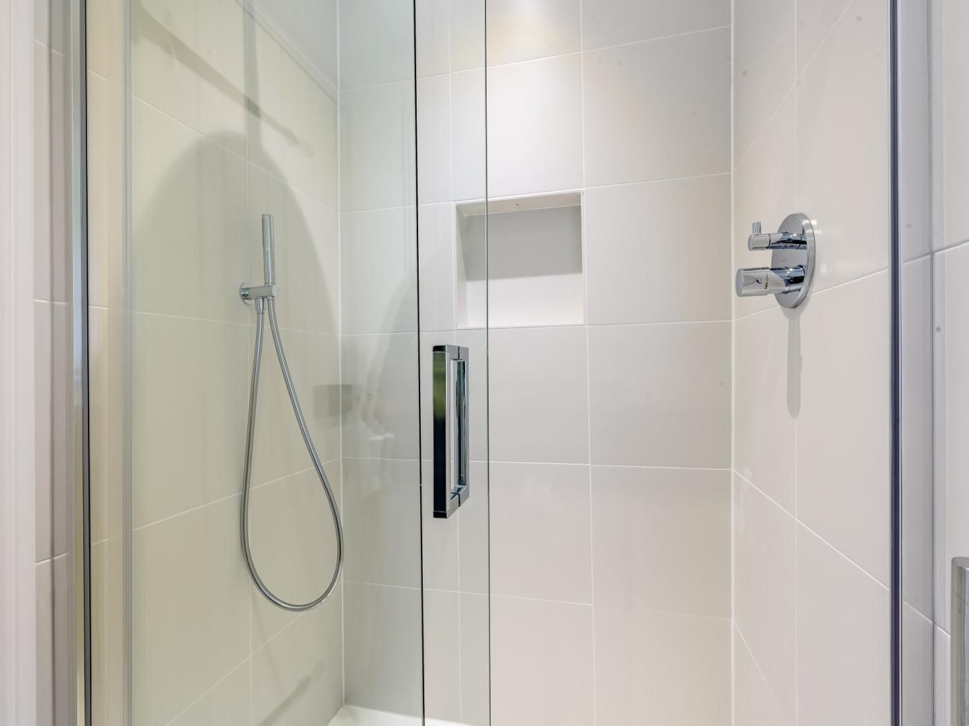 A modern shower with a glass door, chrome fixtures, and a clear showerhead.