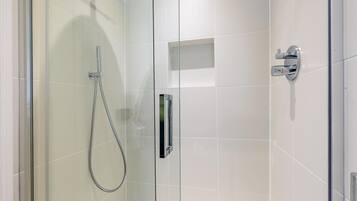 A modern shower with a glass door, chrome fixtures, and a clear showerhead.