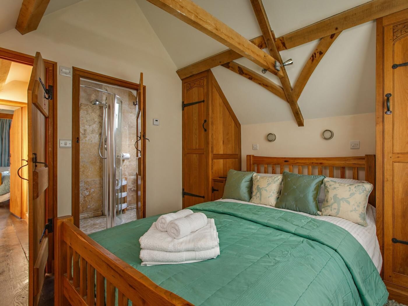 Une chambre avec un lit en bois, une literie verte, une armoire en bois et un espace douche.