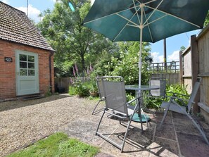 A patio with a table and chairs, a green umbrella, and a brick building with a door. - 1 Bed in King's Lynn (oc-73108) (West Rudham)