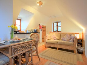 Un salon chaleureux avec un coin repas, un canapé en osier, une table à manger avec des chaises, et une cuisine en arrière-plan.