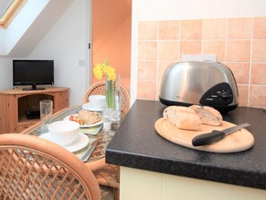 A dining area with a table set for two, a toaster, and a television in the background. - 1 Bed in King's Lynn (oc-73108) (West Rudham)