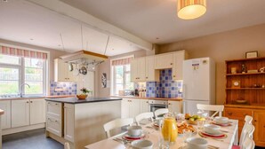 A modern kitchen with white cabinets, a central island, and a dining area set for six. - 5 Bed in Hunstanton (oc-kt185) (Sedgeford)