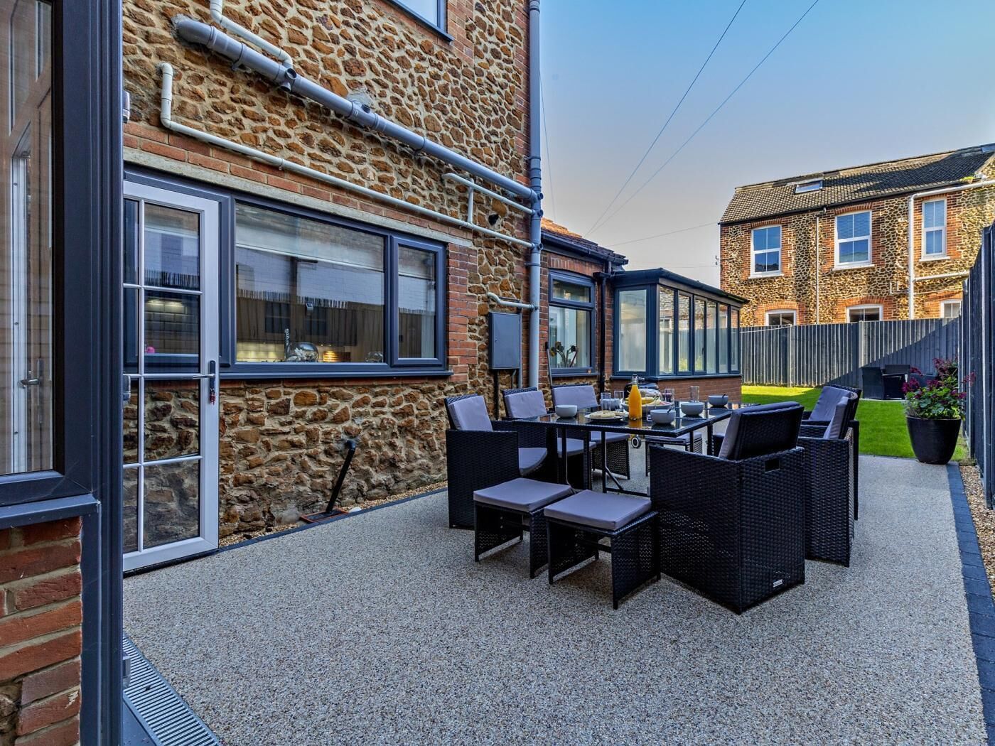 An outdoor patio with a table and chairs, a stone wall, and a brick building in the background.