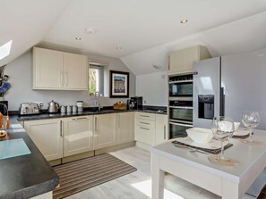 A modern kitchen with a dining area, featuring a built-in oven, a refrigerator, and a window with a view. - 1 Bed in Crieff (oc-58797) (Saint Fillans)