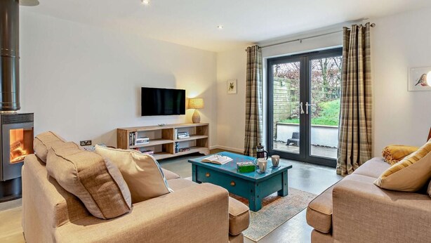 Ein Wohnzimmer mit Kamin, Sofa, Couchtisch, Fernseher und Blick durch eine Glastür.