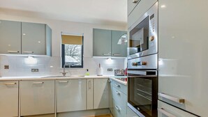 Eine moderne Küche mit hellen Schränken, einem eingebauten Backofen und einem Fenster mit Blick auf Bäume.