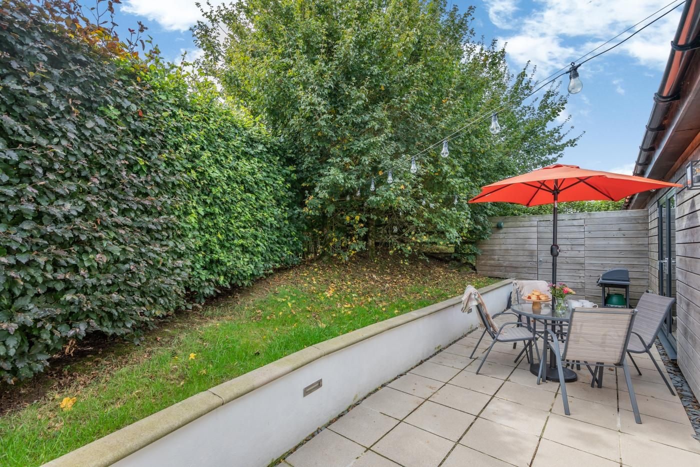 A patio area with a table and chairs, a red umbrella, and a wooden fence.